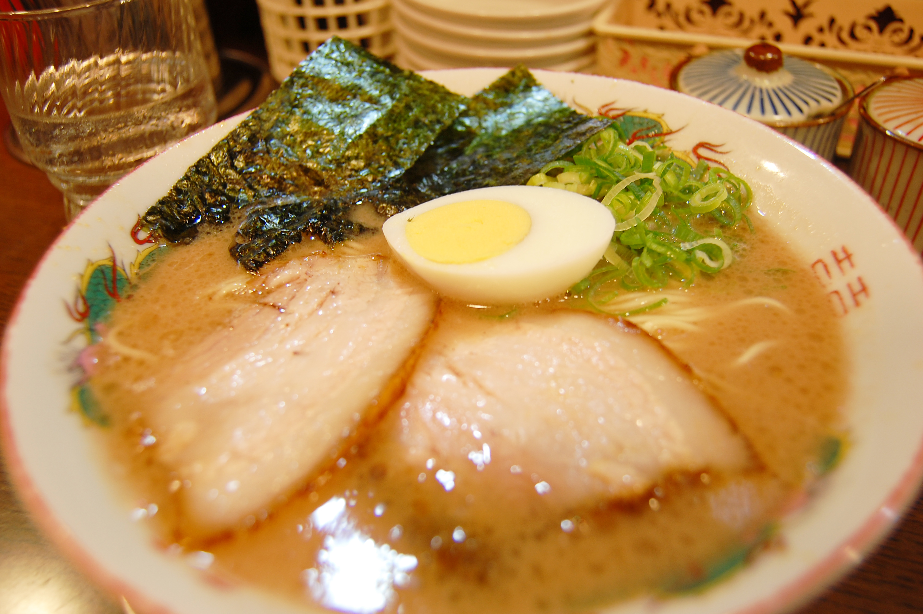 A bowl of shoyu ramen with amber soy broth, three chashu slices, soft-boiled egg and nori